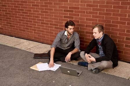 © newsgrape Leo Fasbender und Felix Häusler sitzen mit einem Laptop vor einer Mauer